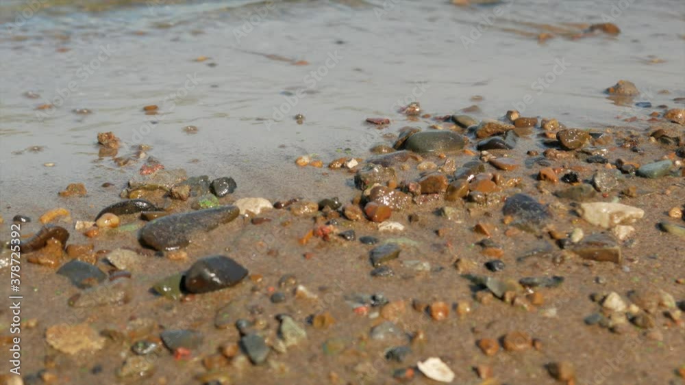 Small waves run over the sandy seashore with small pebbles, close-up Small waves run over the sandy seashore with small pebbles, close-up