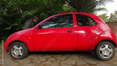 a shot of a person walking around a small red car photo