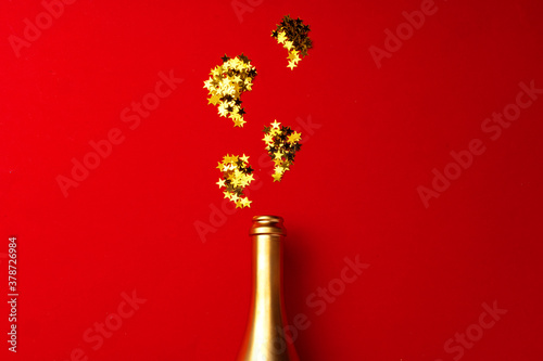 Champagne bottle with sparkling confetti on red background flat lay