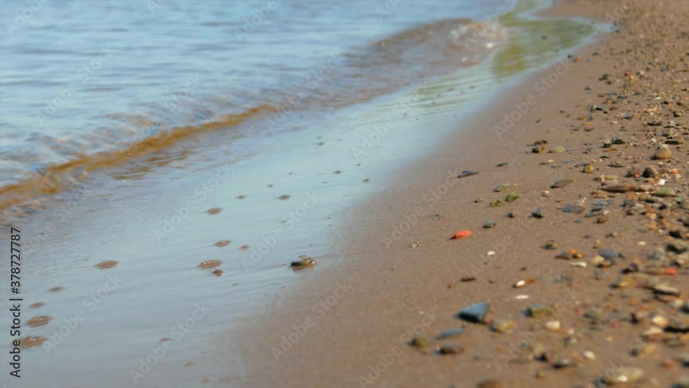 Small waves run over the sandy seashore with small pebbles, close-up Small waves run over the sandy seashore with small pebbles, close-up