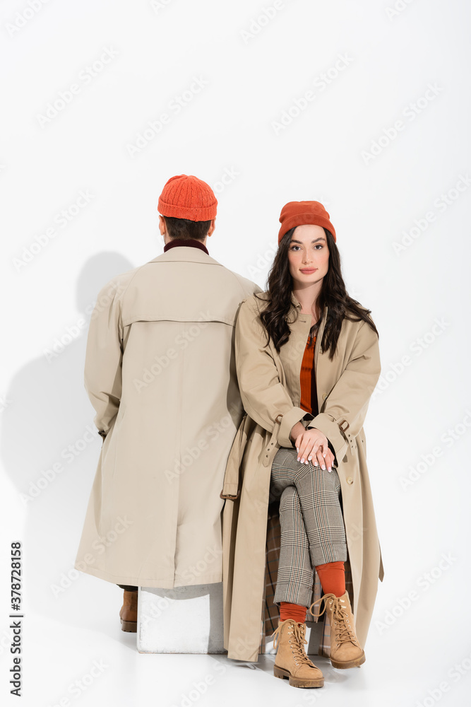 back view of man sitting near young stylish woman in beanie hat on white