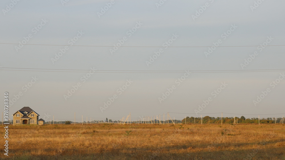a lonely stone house on the edge of an empty field with dried grass in the yellow light of morning or evening time, a farm or ranch with a single dwelling against the backdrop of a southern village