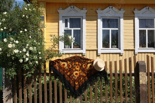 Vintage Pavlovo Posad shawl, straw hat, rural wooden house in Yukhnov town, Russia. Russian folk style in architecture, fashion. Pavlovoposadsky, Pavloposadsky shawl in beautiful russian countryside photo