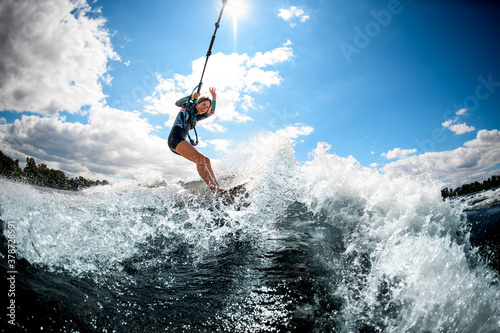 Young active cheerful woman riding on the wake surf holding rope of motorboat