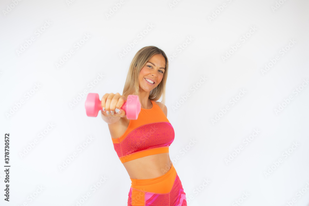 Woman in sportswear showing a pink dumbbell while smiling to the camera Woman in sportswear showing a pink dumbbell while smiling to the camera
