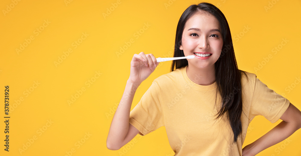 Smile young woman holding white toothbrush in her hand while looking at camera over isolated yellow background with copy space. Good oral and dental health concept. Smile young woman holding white toothbrush in her hand while looking at camera over isolated yellow background with copy space. Good oral and dental health concept.