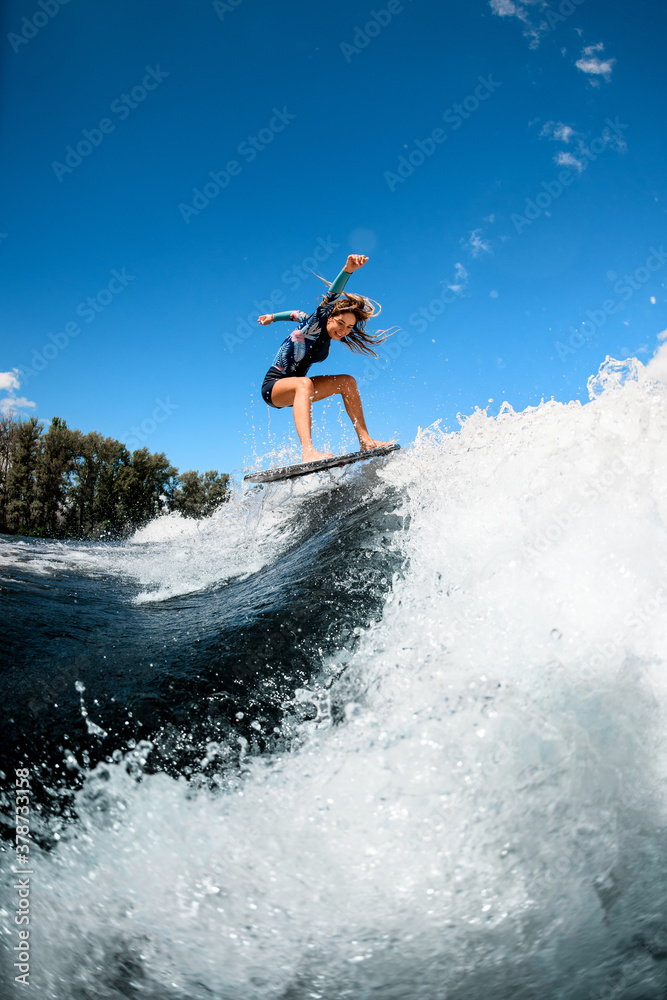 Beautiful young woman skillfully jumping with surf board on wave