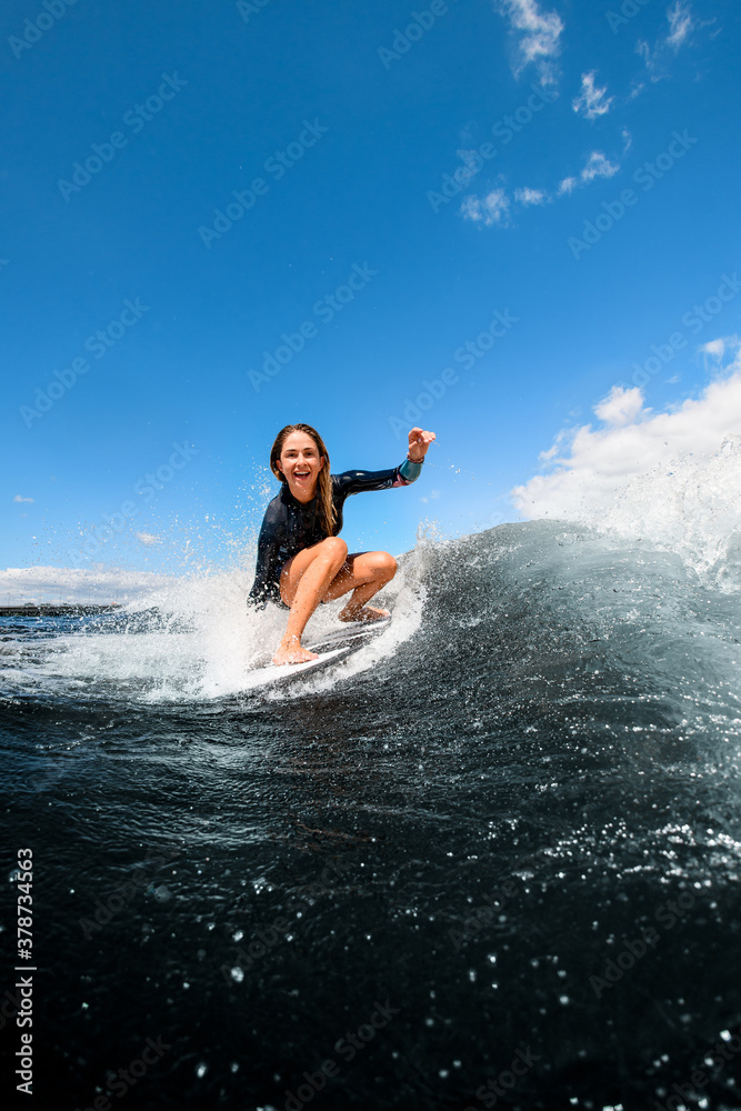 Beautiful view of happy woman sitting on surfboard and riding the wave