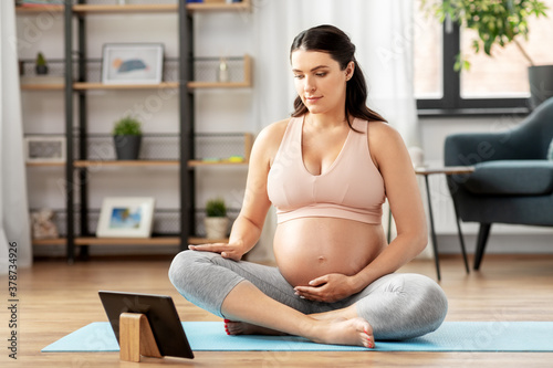sport, fitness and technology concept - happy pregnant woman with tablet pc computer doing yoga at home
