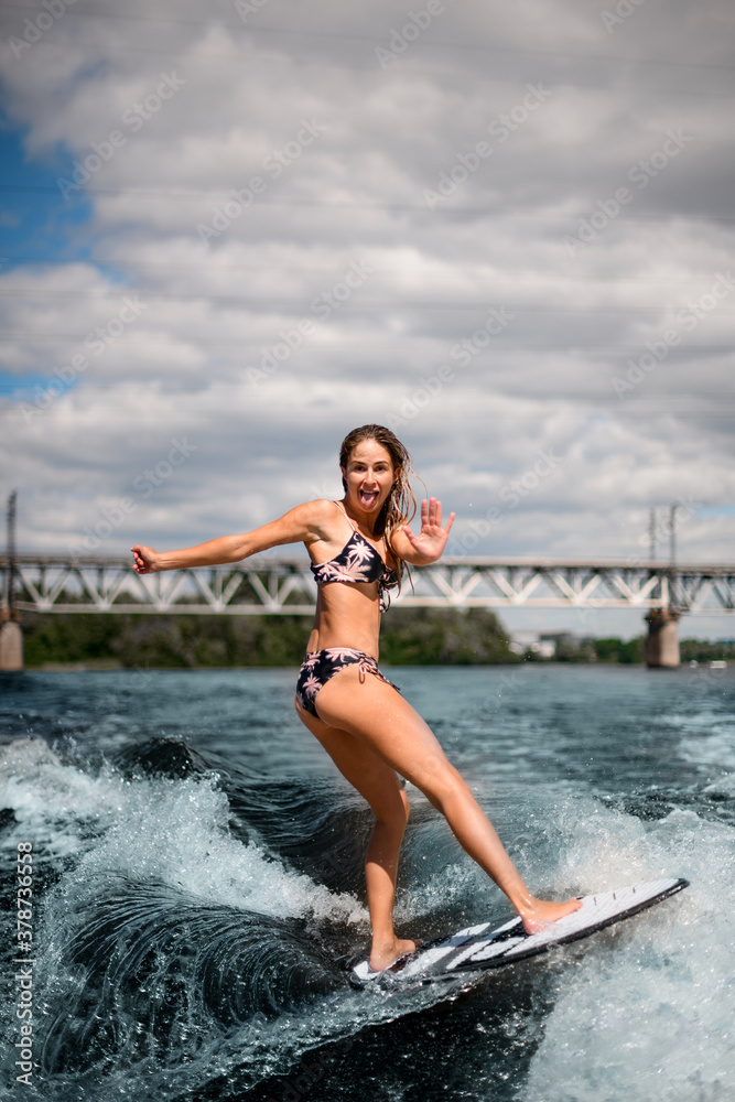 young beautiful woman stand on surfboard and vigorously rides on wave