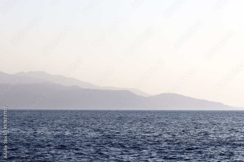 View from the sea to the mountainous islands, coast in the evening. Picturesque seascape, coastline with hills covered by forest in a mist