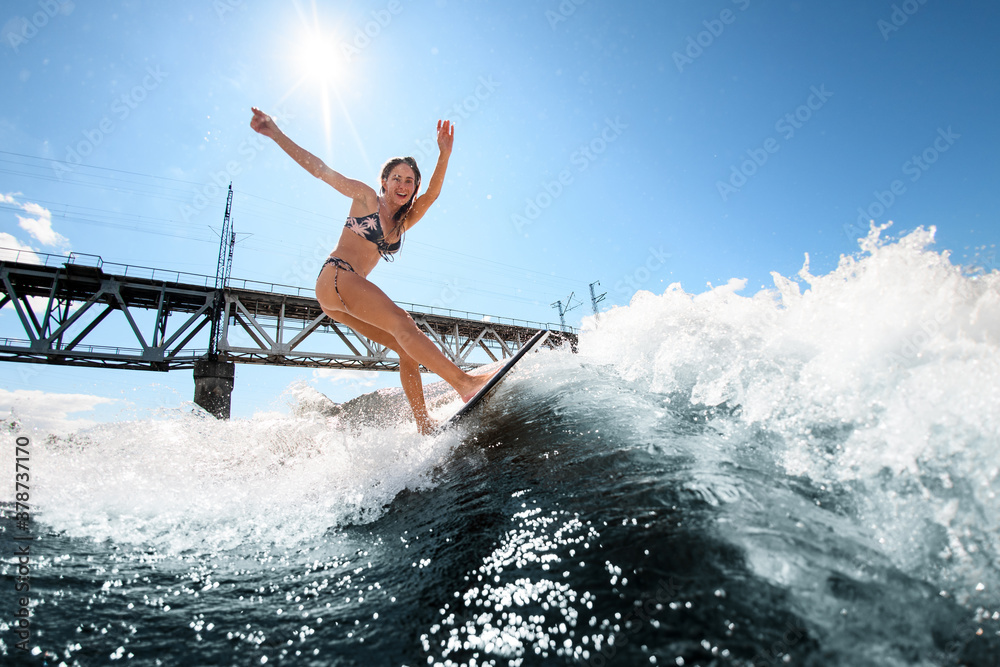 sporty woman on surfboard rides up the wave against the background of the bridge