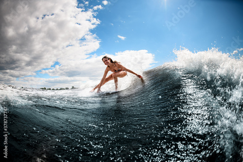 Young woman masterfully rides on surfboard along the wave and touches the water