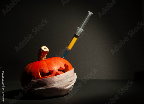 Halloween pumpkin with mask and syringe with yellow liquid, inoculation, on a dark background