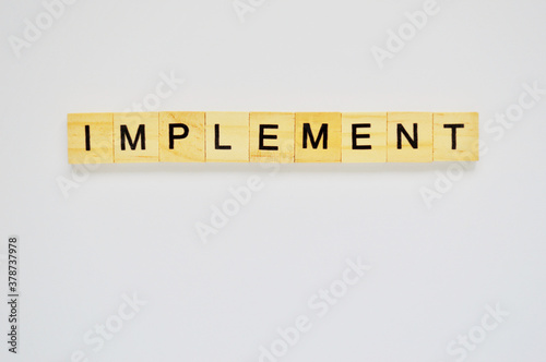 Word implement. Wooden blocks with lettering on top of white background. Top view of wooden blocks with letters on white surface
