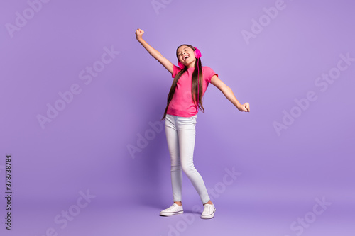 Full length body size photo of little girl singing listening to music with headphones dancing wearing casual outfit isolated on purple color background