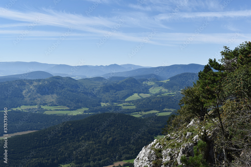 Landschaft mit Hügeln, Wiesen, Felsen, Bergen, blauer Himmel mit zarten Wolken als Hintergrund für Urlaub und Tourismus