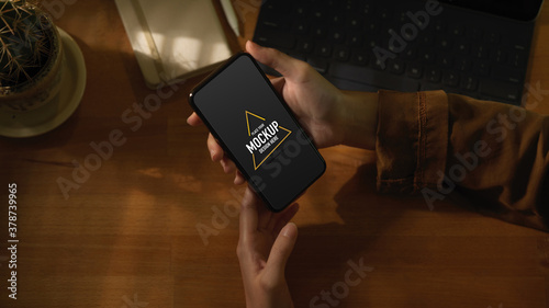 Female hands holding mock up smartphone on worktable