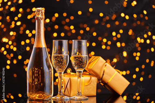 Champagne bottle and wrapped gift on blurred background of Christmas lights