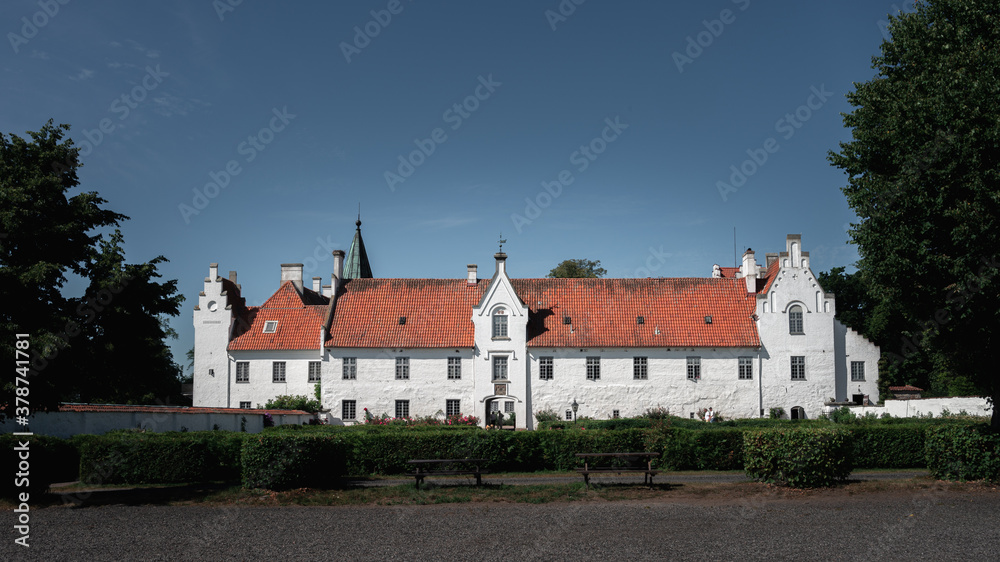 The white facade and orange roof of the medieval Bosjökloster castle on a bright summer day in Sweden