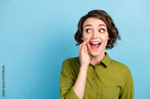 Photo portrait of young pretty girl with short hair telling secret information rumouring gossiping wearing green shirt isolated on blue color background