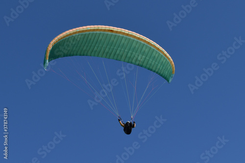 Kiteschirm in Grün und Lachsfarben vor dunkelblauem Himmel mit Kiteflieger
