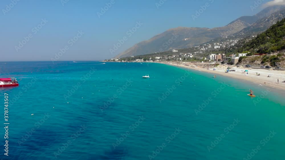 Long sandy beach with umbrellas on shore washed by azure water, anchored boats in Ionian sea Long sandy beach with umbrellas on shore washed by azure water, anchored boats in Ionian sea