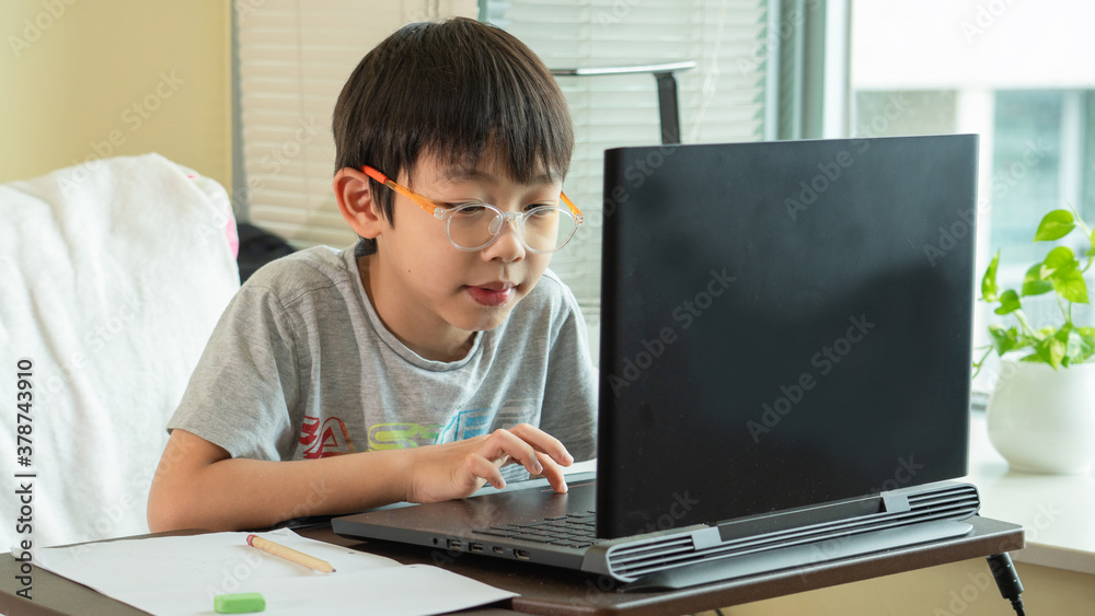 On Asian boy student is learning online class and studying by video call. The happy boy learns english language with laptop at home.New normal.Covid-19 coronavirus, social distancing and staying home. On Asian boy student is learning online class and studying by video call. The happy boy learns english language with laptop at home.New normal.Covid-19 coronavirus, social distancing and staying home.