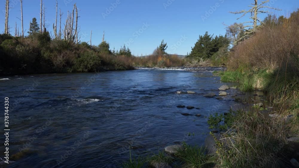 Tranquil Scenery By The River With Dark Blue Water Flowing Under The Clear Sky At Daytime - static slowmo shot Tranquil Scenery By The River With Dark Blue Water Flowing Under The Clear Sky At Daytime - static slowmo shot