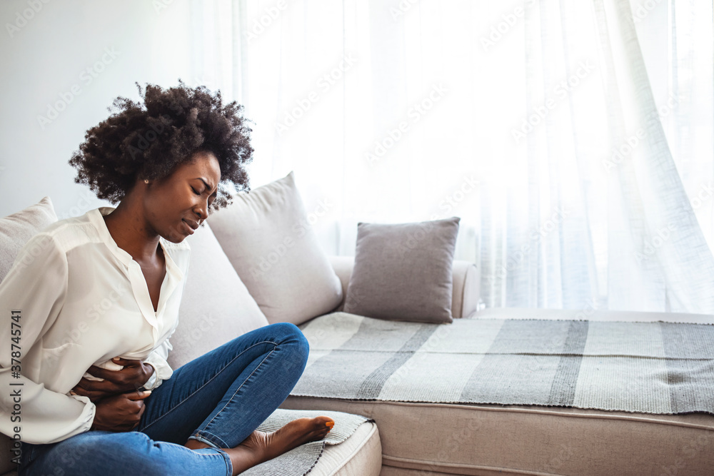 Sad, upset, unhappy woman holding hands on stomach suffering from abdominal pain with close eyes, having menstrual period, food poisoning, gastritis, diarrhea, feeling unwell sitting in livingroom Sad, upset, unhappy woman holding hands on stomach suffering from abdominal pain with close eyes, having menstrual period, food poisoning, gastritis, diarrhea, feeling unwell sitting in livingroom