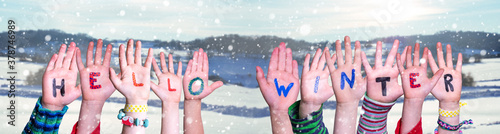 Children Hands Building Colorful English Word Hello Winter. Snowy Winter Background With Snowflakes