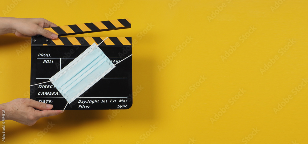 Black with yellow Clapper board or movie slate with face mask. it use in video production and cinema industry on yellow background.