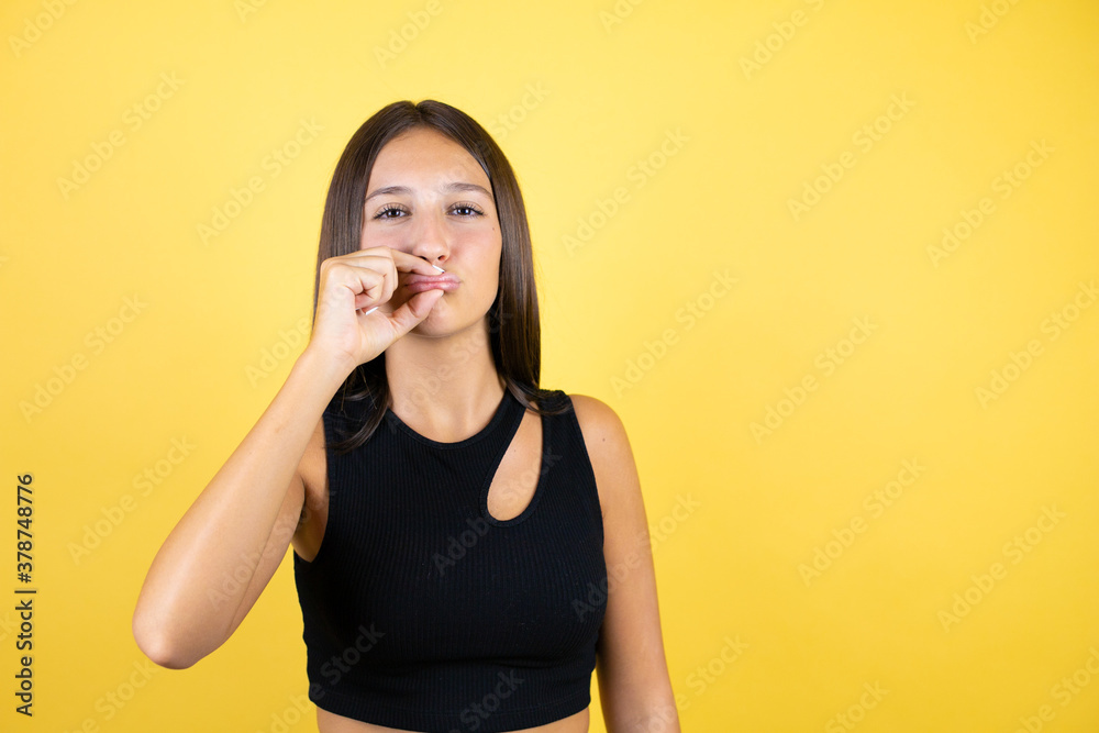 Beautiful young girl kid over isolated yellow background mouth and lips shut as zip with fingers. Secret and silent, taboo talking Beautiful young girl kid over isolated yellow background mouth and lips shut as zip with fingers. Secret and silent, taboo talking