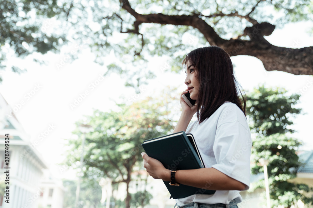 Fototapeta premium Side view - University student talking on the phone at park.