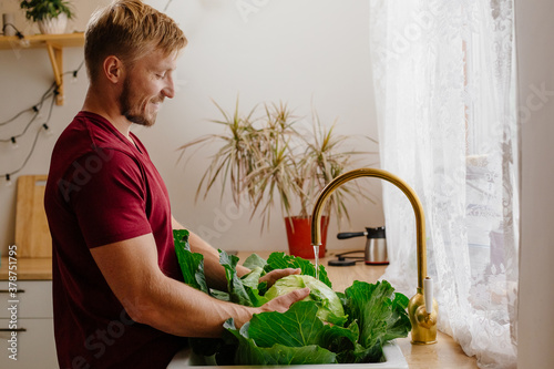 Portrait of a thirty-year-old man of European appearance at home in the kitchen. A man washes a large fresh cabbage in the sink. Agriculture and horticulture.