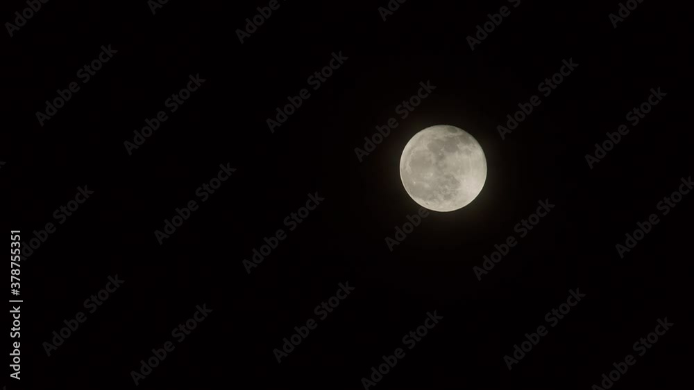 Full moon slowly rising against dark sky through light clouds. Full moon slowly rising against dark sky through light clouds.