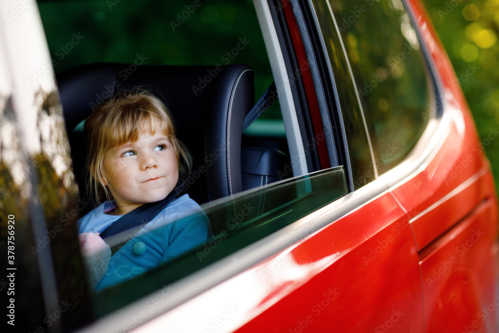 Adorable toddler girl sitting in car seat, holding plush soft toy and looking out of the window on nature and traffic. Little kid traveling by car. Child safety on the road. Family trip and vacations Adorable toddler girl sitting in car seat, holding plush soft toy and looking out of the window on nature and traffic. Little kid traveling by car. Child safety on the road. Family trip and vacations