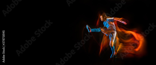 Champion. Football or soccer player on black studio background in mixed light. Young male sportive model training in action. Kicking ball, attacking, catching. Concept of sport, competition. Flyer