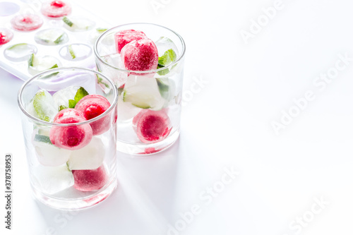 Cocktail glasses with berries in ice cubes on white table copy space