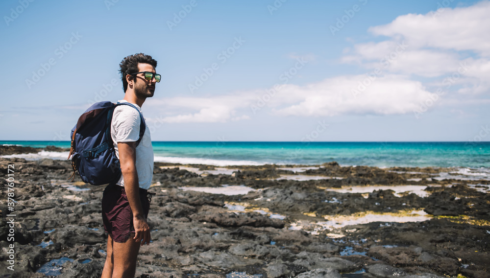 Man with backpack enjoying sunny day on rocky coast