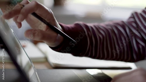 Woman working on her ipad while holding a pencil. Close up and background out of focus.