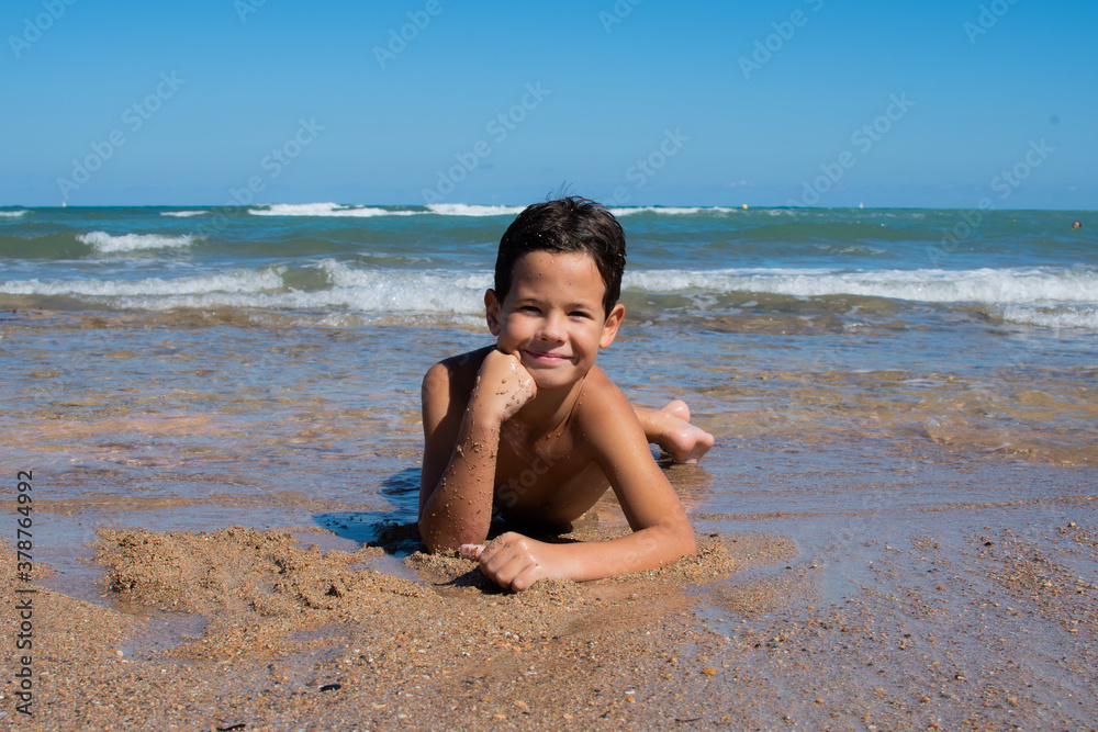 Little boy lying on the sand on the beach by the sea