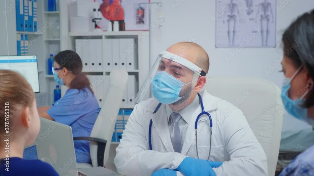 Child and doctor with protection mask talking and laughing in medical office during coronavirus. Physician specialist in medicine providing health care services consultation treatment in hospital. Child and doctor with protection mask talking and laughing in medical office during coronavirus. Physician specialist in medicine providing health care services consultation treatment in hospital.