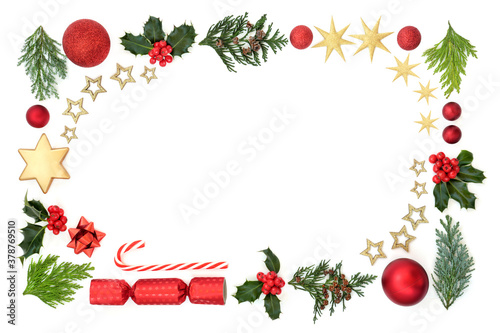 Christmas border composition with winter holly & flora with bauble decorations and symbols of the festive season on white background. Flat lay, top view, copy space.