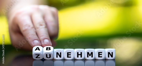Hand turns dice and changes the German expression "zunehmen" (gain weight) to "abnehmen" (lose weight).