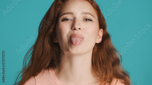 Portrait of attractive redhead girl showing tongue on camera isolated. Childish mood expression