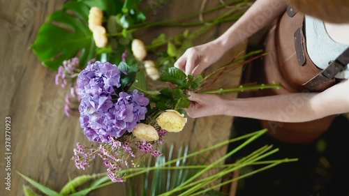 Young florist woman in leather apron holding beautiful chrysanthemum and roses flowers making bouquet in shop. Top view. Small business and plants concept.