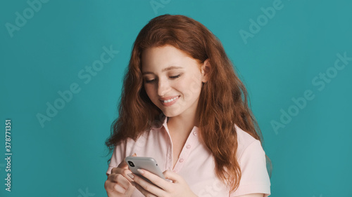 Pretty smiling girl happily using smartphone over colorful background © Anton