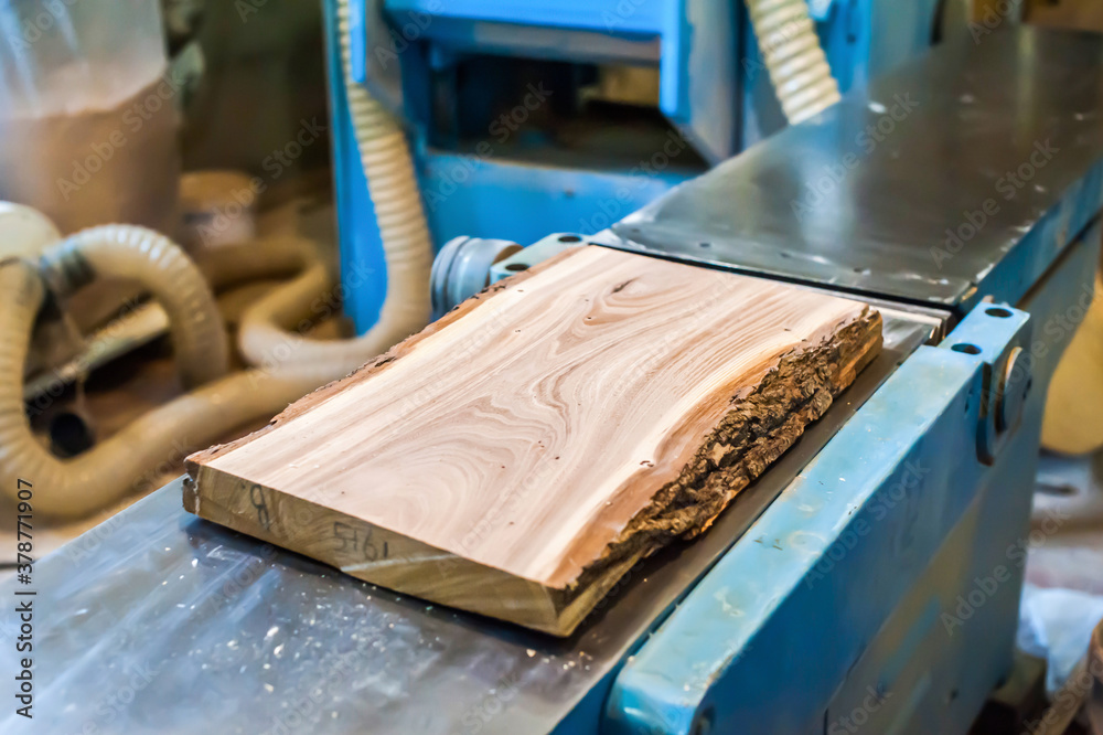 Wooden board slab lies on a large woodworking machine in a carpentry workshop