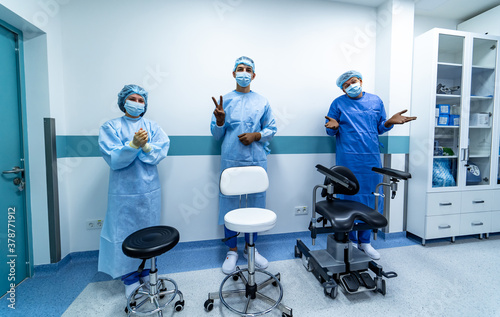 Three office chairs in hospital hall. Three doctors standing behind. Medics in scrubs.